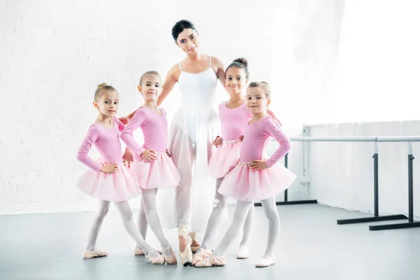 Profesora de ballet con lindas bailarinas sonriendo a la cámara en la escuela de ballet - foto de stock