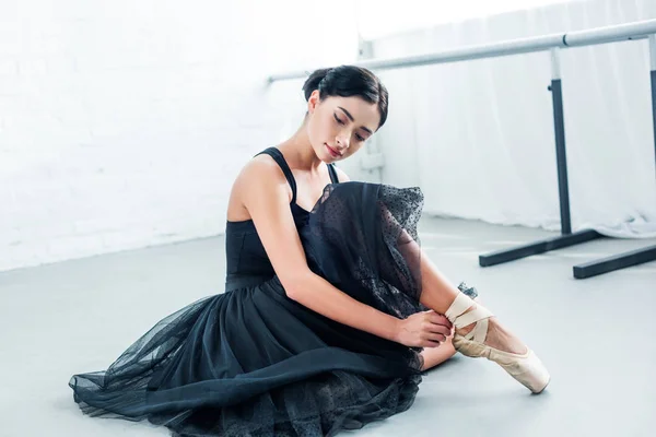 Beautiful tender young ballerina sitting and wearing pointe — Stock Photo