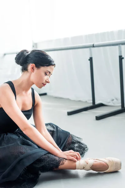 Beautiful tender young ballerina sitting and tying pointe — Stock Photo