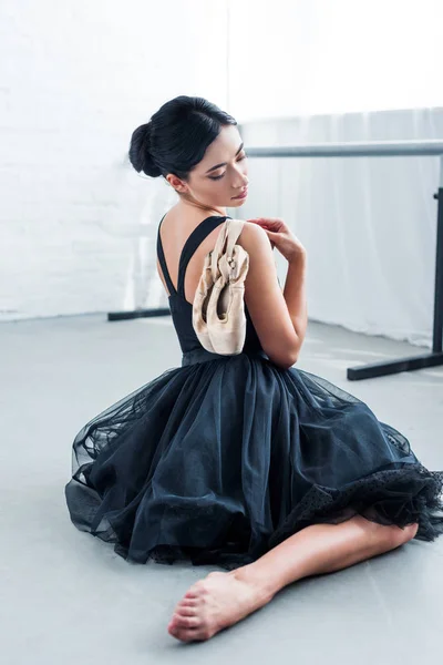 Hermosa tierna joven bailarina sosteniendo zapatos puntiagudos y sentado en el estudio de ballet - foto de stock