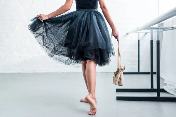 Tiro cortado de bailarina em tutu preto segurando sapatos pointe no estúdio de balé — Fotografia de Stock