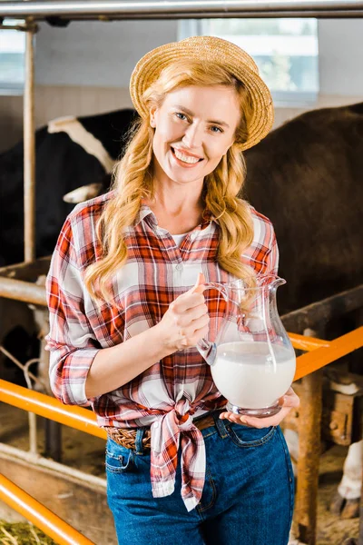 Portrait of smiling attractive farmer holding jug of milk in stable and looking at camera — Stock Photo