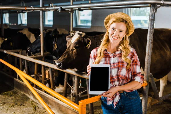 Attractive farmer in straw hat showing tablet with blank screen in stable — Stock Photo