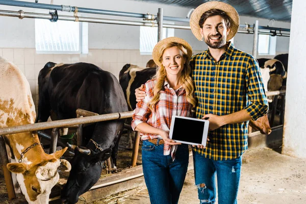 Sonriente pareja de agricultores sosteniendo tableta con pantalla en blanco en establo - foto de stock