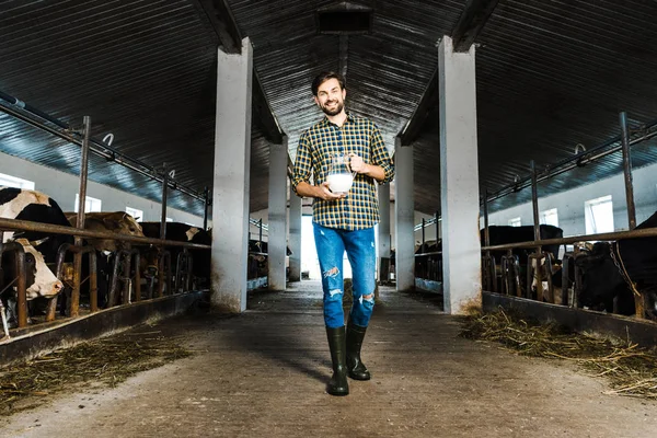 Bel contadino che cammina in stalla con brocca di latte — Foto stock
