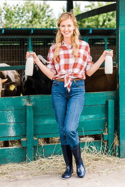 Attractive farmer showing bottles of cow milk near stable — Stock Photo