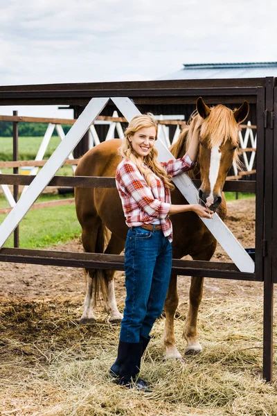 Attractive farmer palming horse in stable — Stock Photo