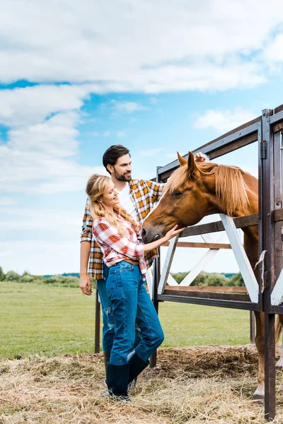 Casal de fazendeiros felizes palming cavalo no estábulo — Fotografia de Stock