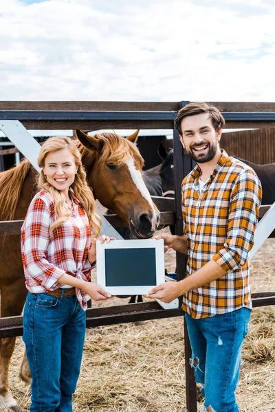 Feliz pareja de agricultores sosteniendo pizarra en estable - foto de stock