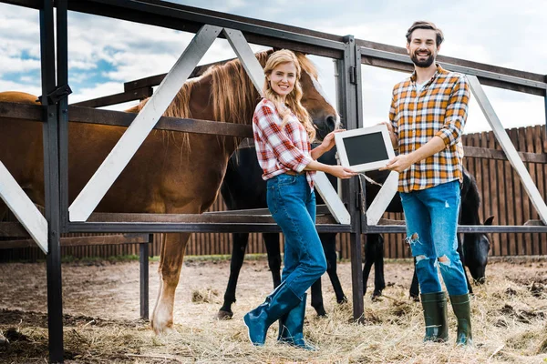 Smiling couple of farmers holding blackboard in stable — Stock Photo