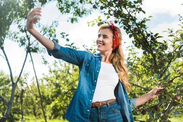 Atractivo agricultor tomando selfie con teléfono inteligente en el jardín de manzanas en la granja - foto de stock
