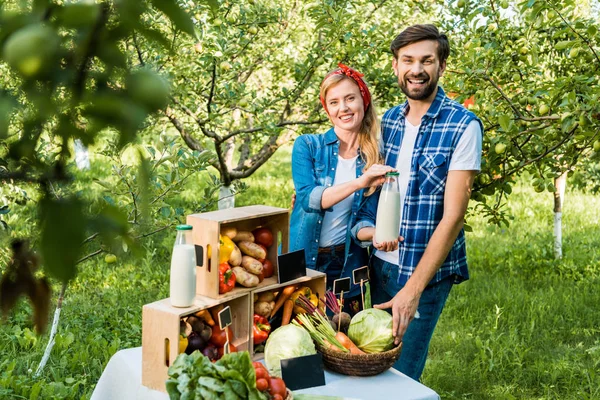 Coppia di agricoltori che mostrano una bottiglia di latte al mercato contadino — Foto stock