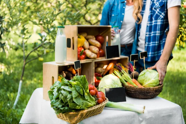 Cropped image of couple of farmers standing near boxes with ripe vegetables at farmer market — Stock Photo