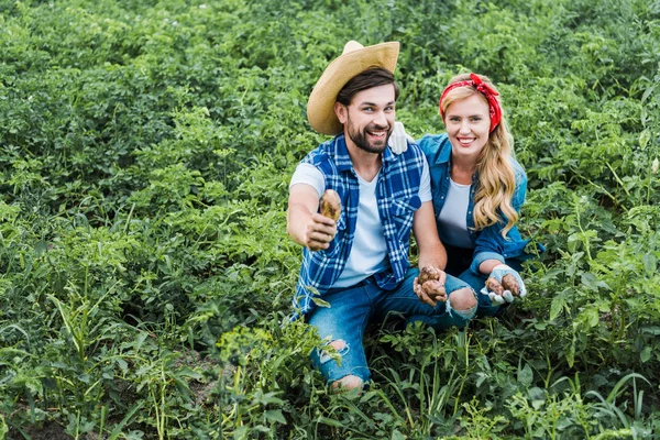 Happy couple of farmers showing potatoes in field at farm — Stock Photo