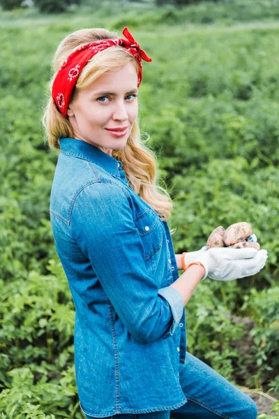 Attraktive Bäuerin mit reifen Kartoffeln auf dem Feld am Hof und Blick in die Kamera — Stockfoto