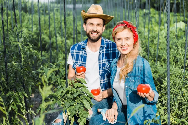 Feliz pareja de agricultores sosteniendo tomates maduros en el campo en la granja y mirando a la cámara - foto de stock