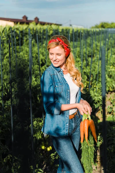 Attractive farmer holding organic carrots in field at farm — Stock Photo