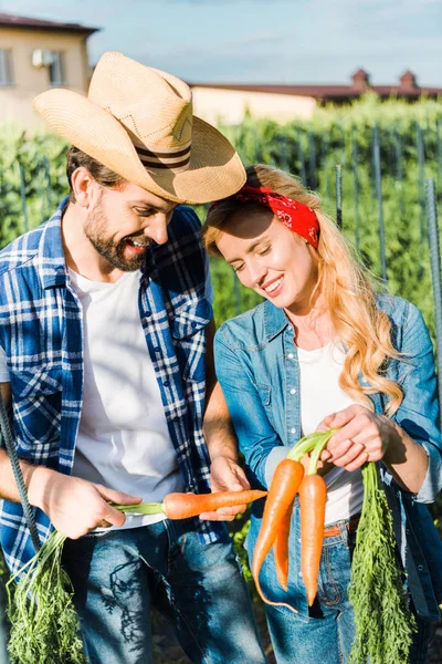 Smiling couple of farmers holding organic carrots in field at farm — Stock Photo