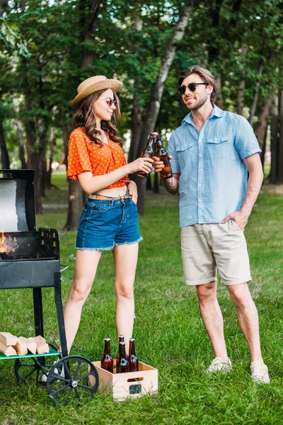 Élégant couple cliquetis bouteilles de bière pendant le barbecue dans le parc — Photo de stock
