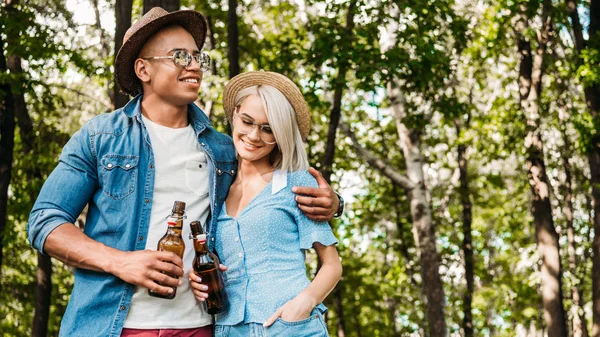 Retrato de casal multirracial sorridente com cerveja no parque de verão — Fotografia de Stock