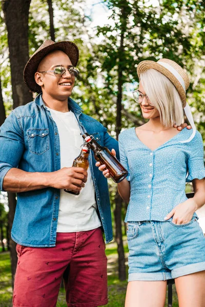 Retrato de casal multirracial clinking garrafas de cerveja no parque de verão — Fotografia de Stock