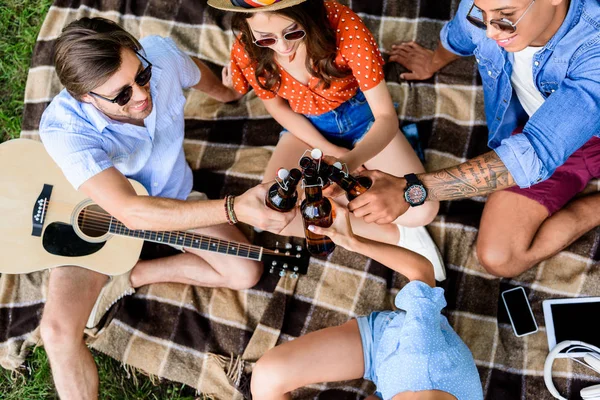 Vista aérea de amigos multiculturais batendo garrafas de cerveja enquanto descansa sobre cobertor no parque — Fotografia de Stock