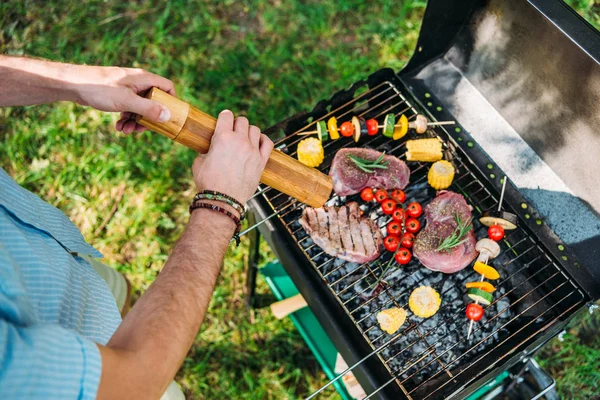 Tiro cortado do homem com moedor cozinhar alimentos na grelha durante o churrasco no parque — Fotografia de Stock