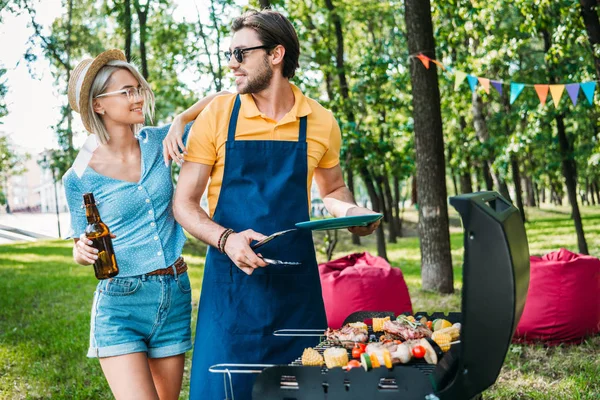 Retrato de pareja alegre teniendo barbacoa en el parque de verano - foto de stock