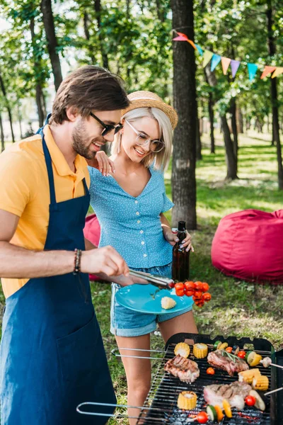 Vista lateral de pareja alegre teniendo barbacoa en parque de verano - foto de stock