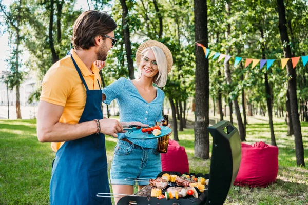 Alegre pareja teniendo barbacoa en verano parque - foto de stock