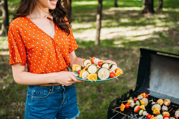 Colpo ritagliato di donna che tiene piatto con verdure grigliate durante il barbecue nel parco — Foto stock