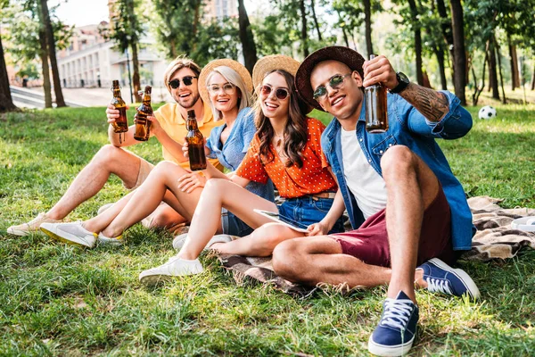 Fröhliche multirassische Freunde mit Bier auf Decke im Sommerpark — Stockfoto