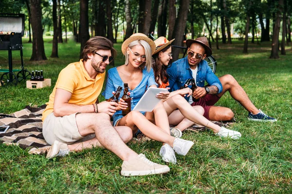 Interracial friends with beer and table resting in summer park — Stock Photo