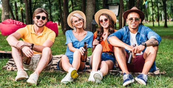 Amigos multirraciales felices con cerveza descansando sobre una manta en el parque de verano - foto de stock