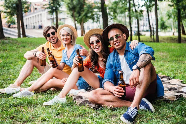 Amigos multirraciales felices con cerveza descansando sobre una manta en el parque de verano - foto de stock
