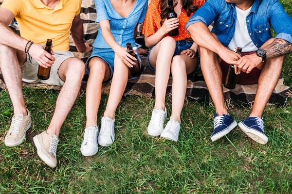 Partial view of interracial friends with bottles of beer resting on blank in park — Stock Photo