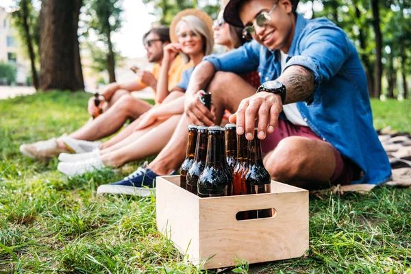 Foco seletivo do homem afro-americano levando garrafa de cerveja com amigos perto no parque — Fotografia de Stock