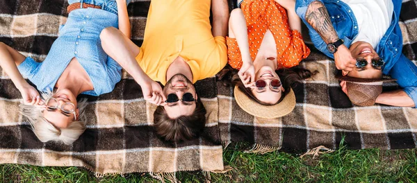 Overhead view of interracial friends in sunglasses resting on blanket in park — Stock Photo