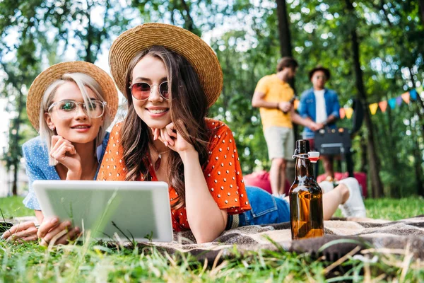 Belles femmes utilisant tablette tandis que les hommes multiethniques cuisiner des aliments sur le gril derrière — Photo de stock