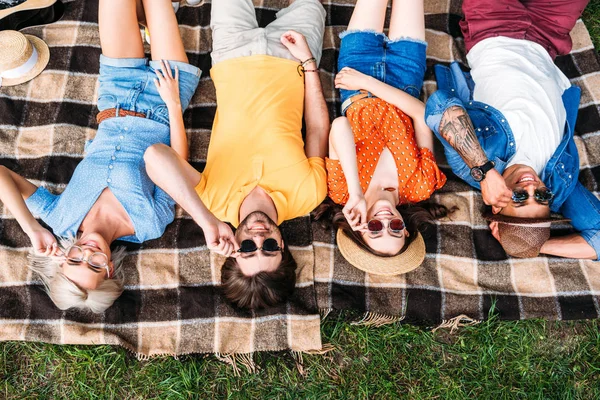 Overhead view of interracial friends in sunglasses resting on blanket in park — Stock Photo