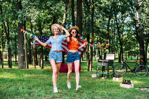 Mujeres felices con bandera americana corriendo en el parque - foto de stock