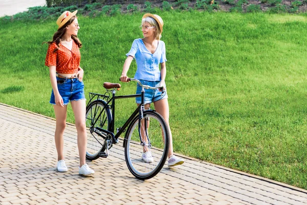 Молодые женщины в шляпах и на велосипеде ходят по улице — стоковое фото