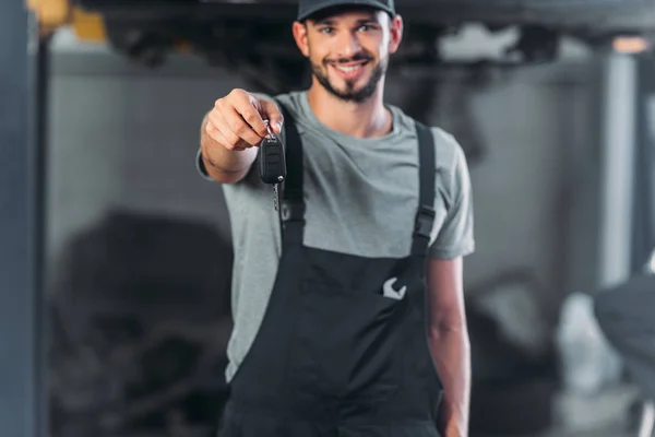 Mecánico sonriente sosteniendo la llave del coche en taller de reparación de automóviles - foto de stock