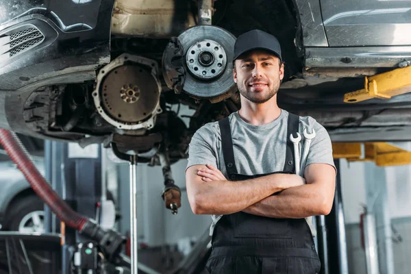 Obrero sonriente posando con brazos cruzados en taller mecánico de automóviles - foto de stock