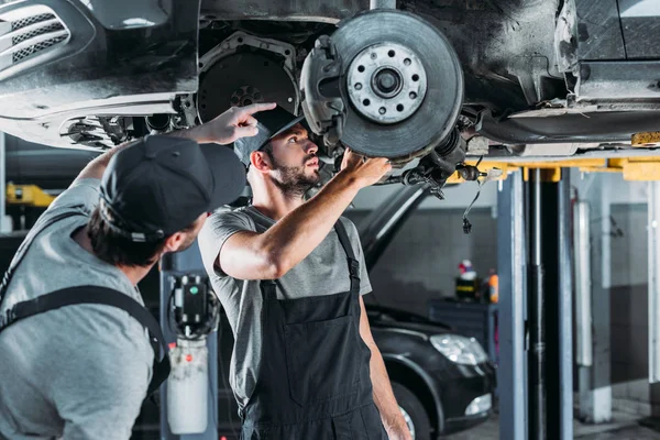 Auto mechanics repairing car without wheel in workshop — Stock Photo