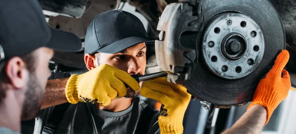 Professional mechanics repairing car without wheel in workshop — Stock Photo