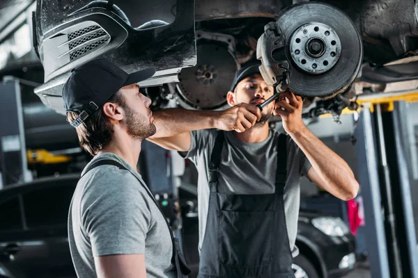 Professional mechanics repairing car without wheel in auto repair shop — Stock Photo