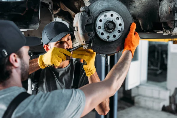 Professionelle Ingenieure reparieren Auto ohne Rad in Mechanikerwerkstatt — Stockfoto