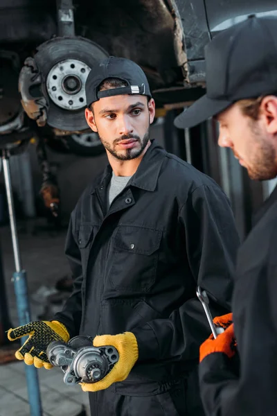 Professional mechanics in uniform working with car and tools in workshop — Stock Photo