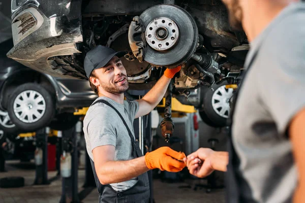 Ouvriers professionnels réparation de voiture sans roue dans l'atelier de mécanique — Photo de stock